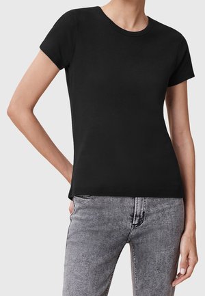 Personne portant un t-shirt noir ajusté à manches courtes et un jean en denim gris clair, debout avec une main sur la hanche et l'autre détendue.