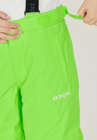 Pantaloni da sci verde neon con cintura regolabile in Velcro, dotati di tasche laterali e un logo bianco "ZIGZAG" sulla parte inferiore della gamba.