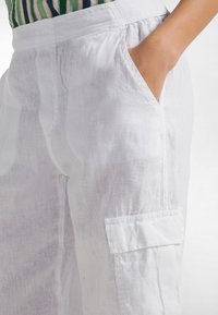 Białe lniane spodnie z boczną kieszenią, luźnym krojem i fakturowaną powierzchnią, prezentujące lekką, przewiewną jakość tkaniny.