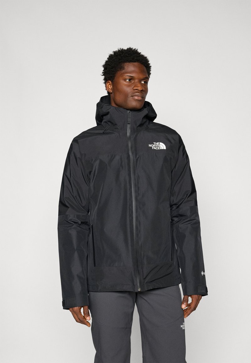 Chaqueta negra impermeable con cierre de cremallera, capucha ajustable y logotipo en el pecho. Presenta mangas largas y una textura suave y ligera.