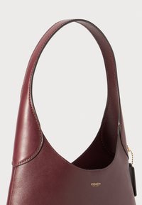 Burgundy leather handbag with a smooth finish, curved handle, and subtle logo detail; unstructured design with no visible hardware accents.