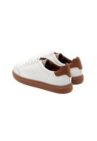 Weiße Leder-Sneaker mit einem Akzent aus braunem Leder an der Ferse, einer strukturierten Gummisohle in Braun und sechs Ösen für die Schnürsenkel.