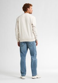 Felpa beige chiaro con una texture a macchie, collo rotondo e polsini a coste, abbinata a jeans blu e sneakers bianche.