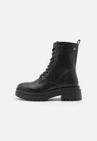 Bottines de combat en cuir noir à lacets avec une semelle épaisse, hauteur cheville, détails de couture et une languette à l'arrière.