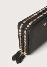 Black textured wallet with two gold zippers, featuring leather zipper pulls and a brand name embossed on the side.