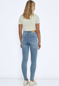 Tynne lyse blå jeans med baklommer, høy midje og et lyst lærpatch p�å midjebåndet. Brukt med en tettsittende lys grønn topp og hvite sneakers.
