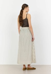 Maxi-Rock mit vertikalen cremefarbenen und dunkelblauen Streifen, elastischem Bund und fließendem Stoff. Kombiniert mit einem braunen Tanktop und braunen Ballerinas.