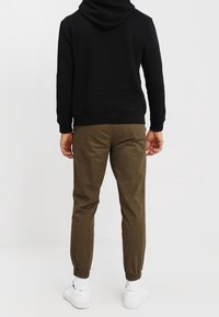 Svart huvtröja, olivgröna avsmalnande joggers med elastiska mudd, och vita sneakers. Släta texturer, minimal detaljer, och avslappnad design.