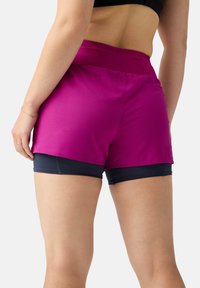 Magenta athletic shorts with a textured surface, featuring a high waist and layered design over navy under-shorts. Reinforced stitching details.