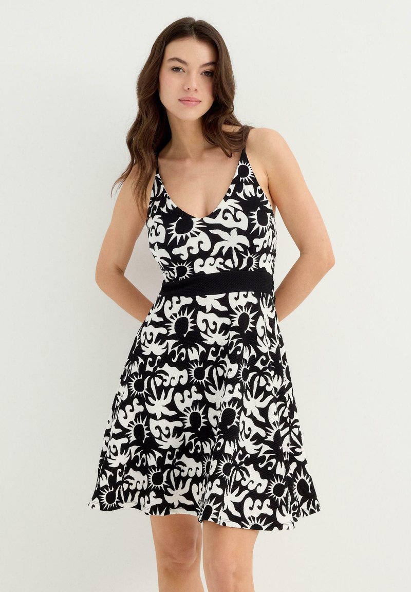 Vestido de estampado floral en blanco y negro, con escote en V, tirantes finos y una cintura ajustada con falda acampanada. Hecho de una tela ligera.