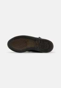 Suela de zapato de goma negra con patrones de textura en el dibujo. Presenta una forma redondeada y ligeras marcas de desgaste, que indican un uso previo.