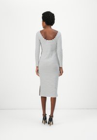 Robe ajustée à rayures avec un dos dégagé, des manches longues et une fente sur le côté. Fabriquée en tissu léger noir et blanc. Présente une silhouette près du corps.