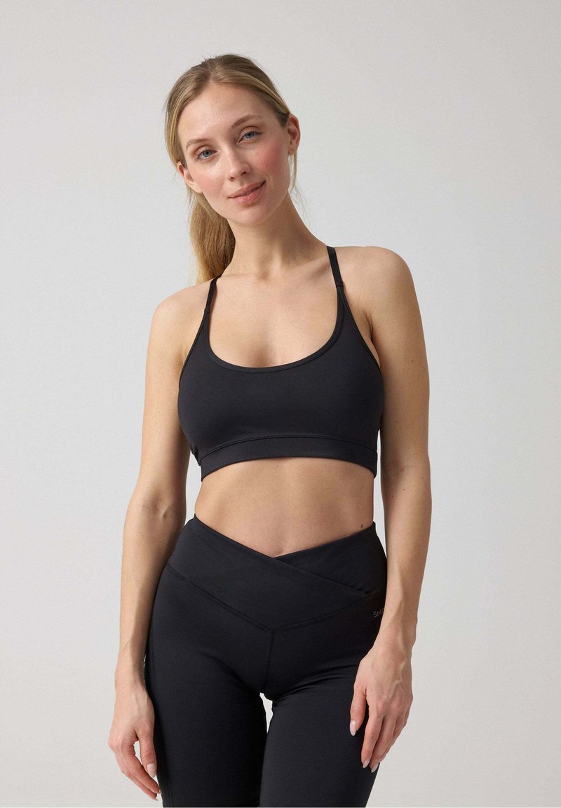 Zwarte sport-bh met een brede band en dunne bandjes, gecombineerd met hoge zwarte legging met een kruisontwerp. Gladde textuur.