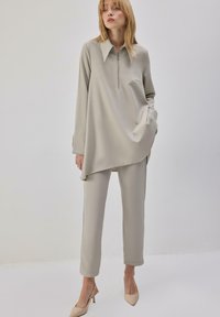 Ensemble lounge gris clair comprenant un haut à col avec fermeture à glissière et un pantalon fuselé. Tissu lisse et doux avec une coupe décontractée et un design minimaliste.