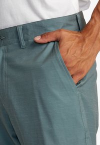 Pantalons bleu clair en tissu texturé, dotés de poches latérales et d'une coupe slim, avec des coutures détaillées le long de la ceinture.