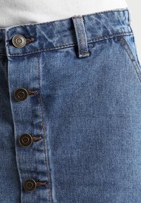 Džínová sukně v světle modré barvě, s knoflíkovým zapínáním na přední straně s kovovými knoflíky, strukturovaným pasem a jemnou texturou.