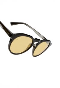 Päikeseprillid mustade tekstuursete raamidega ja kollaka tooniga läätsedega. Omavad kaheksanurkset disaini ning peente kaubamärgi detailidega sangadel.