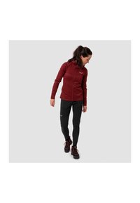 Jachetă zip-up de culoare vișinie cu glugă, pantaloni negri slim-fit și bocanci de drumeție negri. Caracteristici notabile includ accente cu logo și țesătură texturată.