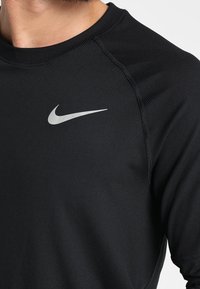 Musta urheilupaita lyhyillä hihoilla, valmistettu sileästä ja hengittävästä kankaasta. Etupuolella vasemmassa yläosassa hopeinen Nike-logo.