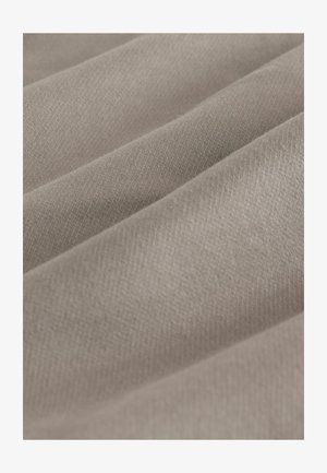 Nahaufnahme von weichem beigen Stoff mit sanften Falten und sichtbarer feiner Webstruktur.