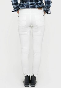 Jeans blancos ajustados con bolsillos traseros cosidos, combinados con botas negras hasta el tobillo. La tela parece suave con un ligero elasticidad.