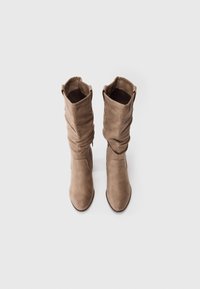 Botas de ante marrón hasta la rodilla con un diseño holgado, punteras afiladas y textura suave. Presenta un puño doblado en la parte superior.
