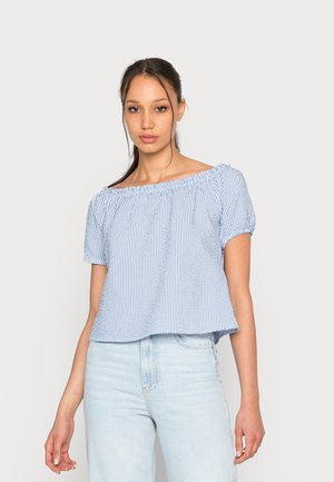 Top listrado azul e branco, com ombros à mostra, mangas curtas bufantes e decote franzido, combinado com jeans azul claro.