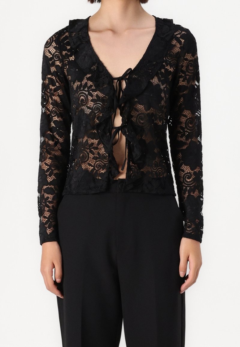 Cardigan in pizzo nero con maniche lunghe, colletto arricciato e chiusura a fiocco sul davanti, che presenta motivi floreali in tutto il capo.