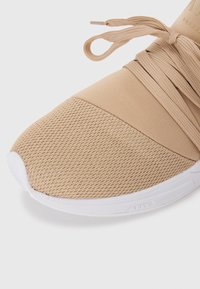 Scarpa sportiva beige con tomaia in mesh testurizzato, fascia in tessuto morbido e suola in gomma bianca. Presenta lacci per una vestibilità sicura.