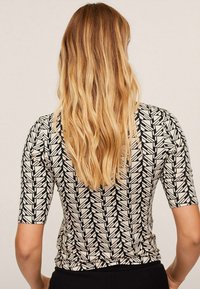 Top de manga corta en beige claro con un patrón geométrico negro. Presenta una forma ajustada y una textura suave. Apto para uso casual.