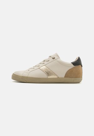 Beige leather sneaker with gold metallic accent, textured brown heel, and black rear piece; features rounded toe and lace-up design.