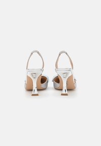 Silver strappy heels with a textured upper, light blue accents, and a shiny metallic heel featuring a unique shape. Back view shown.