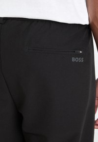 Juodos kelnės su užtrauktuku užpakaliniame kišenėje ir silpnu "BOSS" logotipu. Pagamintos iš lygaus, tamprių audinio, sukurtos patogumui ir judėjimo laisvei.