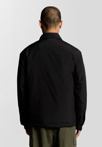 Jachetă exterioară neagră cu un finisaj neted și mat, cu un guler clasic și croială lejeră. Designul este simplu și funcțional.