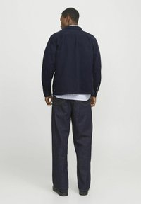 Navy corduroy jacket with long sleeves, button fastening, collar, layered over a white ribbed shirt, paired with dark denim wide-leg pants.