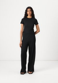 Black ribbed short-sleeve top paired with high-waisted, wide-leg black trousers, featuring a smooth texture and minimalistic design.