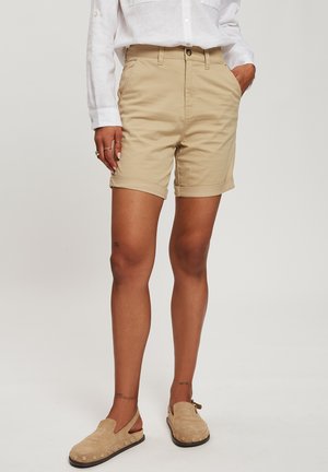 Khaki chino shorts with rolled cuffs, featuring a classic waistband, button closure, and side pockets. Material appears soft and textured.