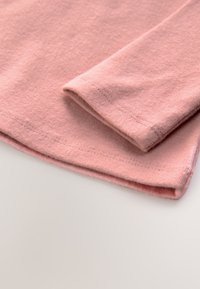 Lichtroze katoenen T-shirtstof met een gladde textuur, voorzien van een gevouwen mouw en zoom met subtiele stikdetails.