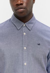Hellblaues Hemd mit Button-Down-Kragen, aus strukturiertem Stoff, mit kontrastierenden Knöpfen und einem kleinen gestickten Logo.