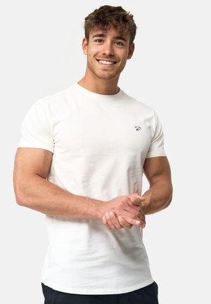 T-shirt en coton blanc avec des manches courtes et un col rond, comportant un petit logo sur la poche gauche. Texture douce. Coupe décontractée.