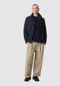 Marineblauwe jas met twee borstzakken, gecombineerd met een donker gebreid sweater en lichtbeige broek. Zwarte chunky schoenen maken de outfit compleet.
