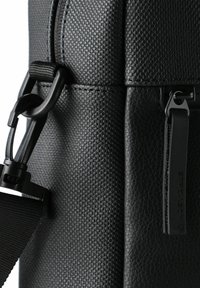 Sort taske med tekstureret læder, glatte accenter og holdbart hardware. Indeholder lynlås og justerbar rem for alsidighed.