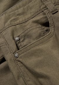 Tejido verde oliva, con un bolsillo plano con remaches de metal, costuras visibles y una textura suave, típico de los pantalones casuales.