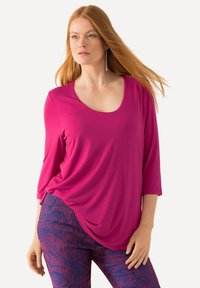 Fuchsia top met een ronde hals en driekwart mouwen, met een drapering ontwerp. Gecombineerd met marineblauwe broeken met een patroon van roze abstracte ontwerpen.