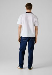 Hvid kortærmet t-shirt med en kontrasterende rød og navy krave, parret med mørkeblå jeans og lyse sko. Enkel design, afslappet pasform.