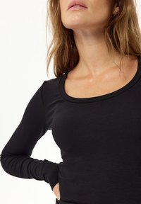 Czarna, prążkowana bluzka z długim rękawem, o okrągłym dekolcie i dopasowanej sylwetce. Materiał wydaje się miękki i ma widoczną teksturę.