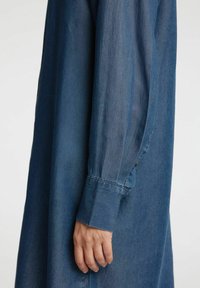 Farkkutakki pitkähihaisena, tummansinisenä, napilla varustetut hihansuut, ja sileä rakenne. Ominaisuuksina istuva ranne ja hieman rento leikkaus.