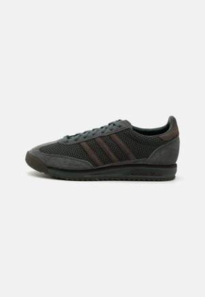 Gray athletic shoes with mesh and suede materials, featuring three dark brown stripes, round laces, and a textured rubber sole.