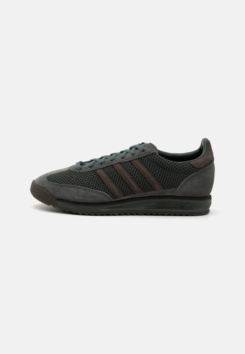 Graue Sportschuhe aus Mesh- und Wildledermaterialien, mit drei dunkelbraunen Streifen, runden Schnürsenkeln und einer strukturierten Gummisohle.