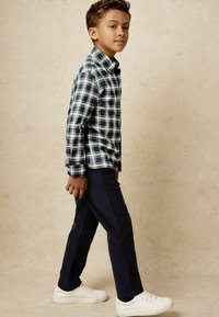 Camisa de cuadros en azul marino y blanco, combinada con pantalones oscuros y zapatillas blancas. Tejido suave y estilo de corte regular.